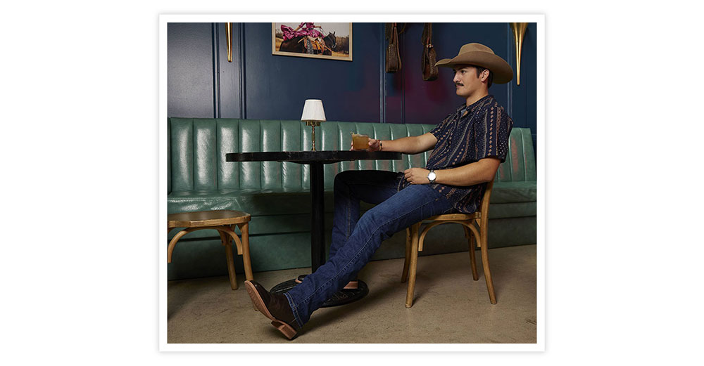 A man wearing Lyle 12” Western boot in brown posing and holding a drink.